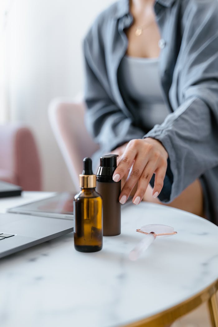 A woman extends her hand to reach skincare bottles and a jade roller on a table, emphasizing self-care and wellness.